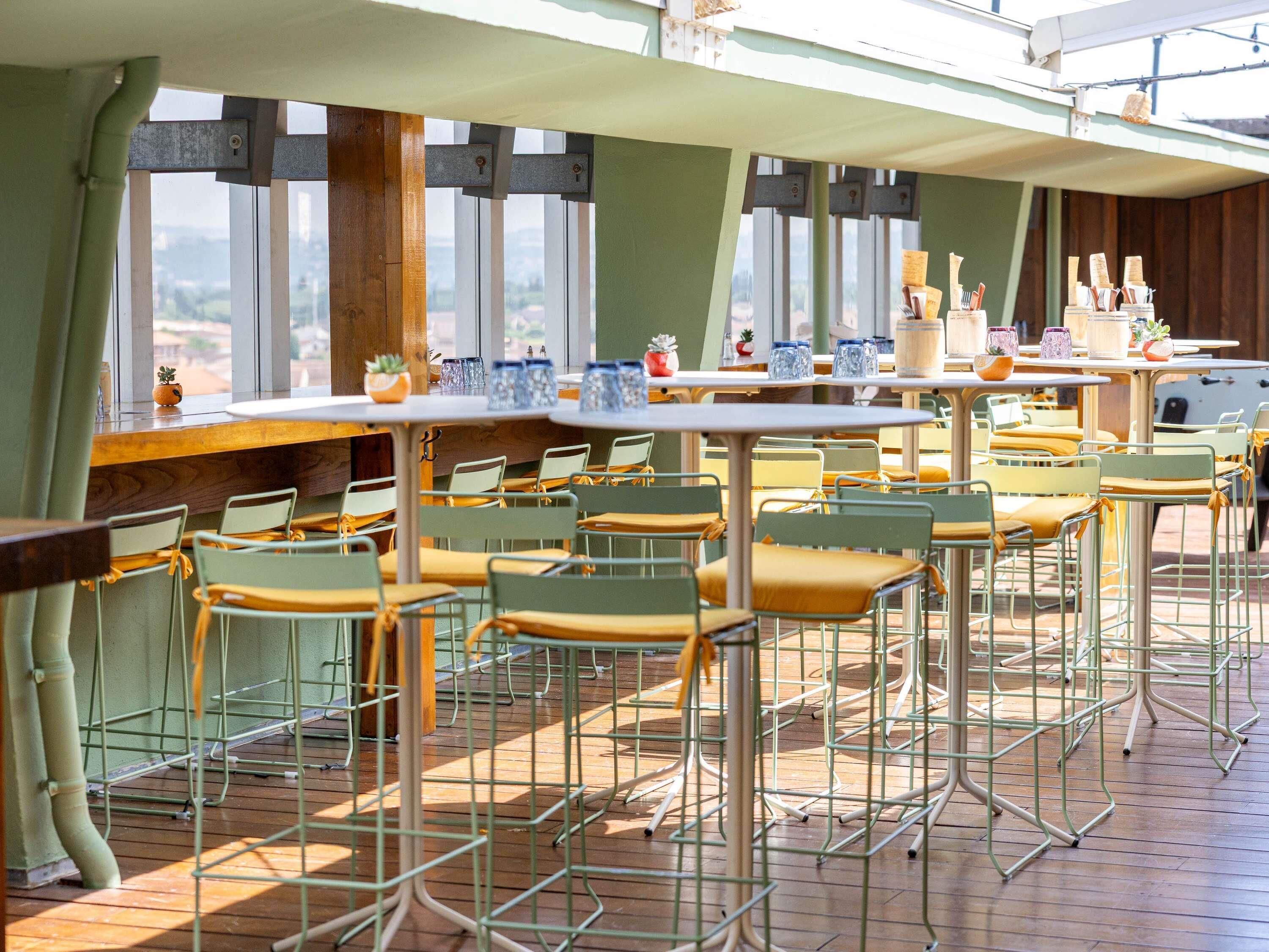 A restaurant with outdoor seating, tables, chairs, and a view through large windows.