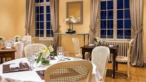 Een eetruimte met ronde tafels, witte tafellinnen en rieten stoelen.