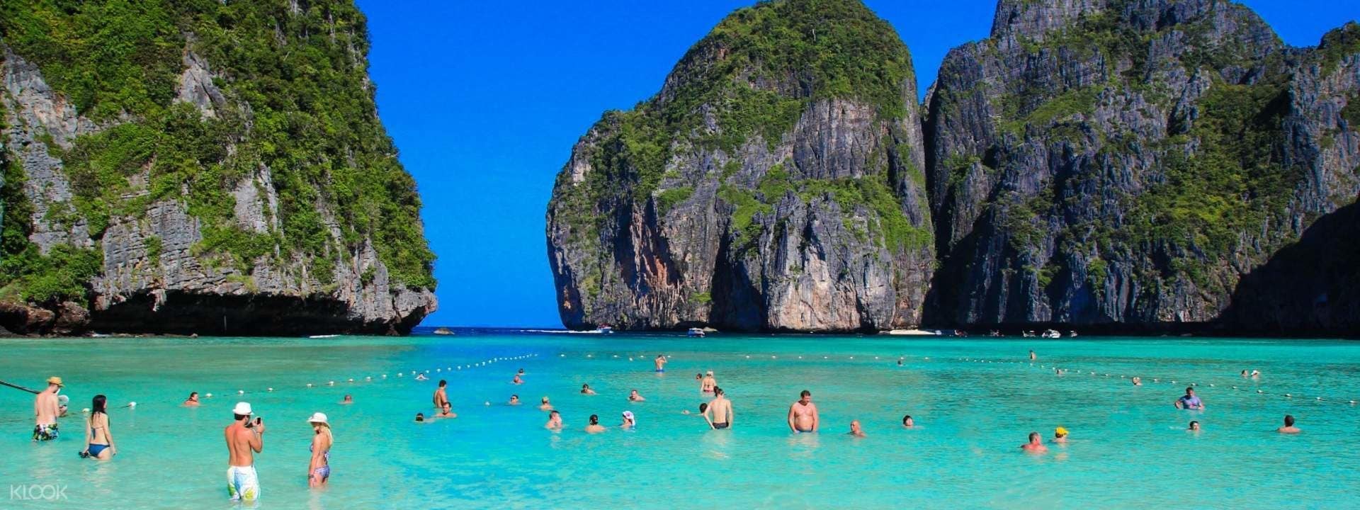 A beach with clear turquoise water and rocky cliffs.