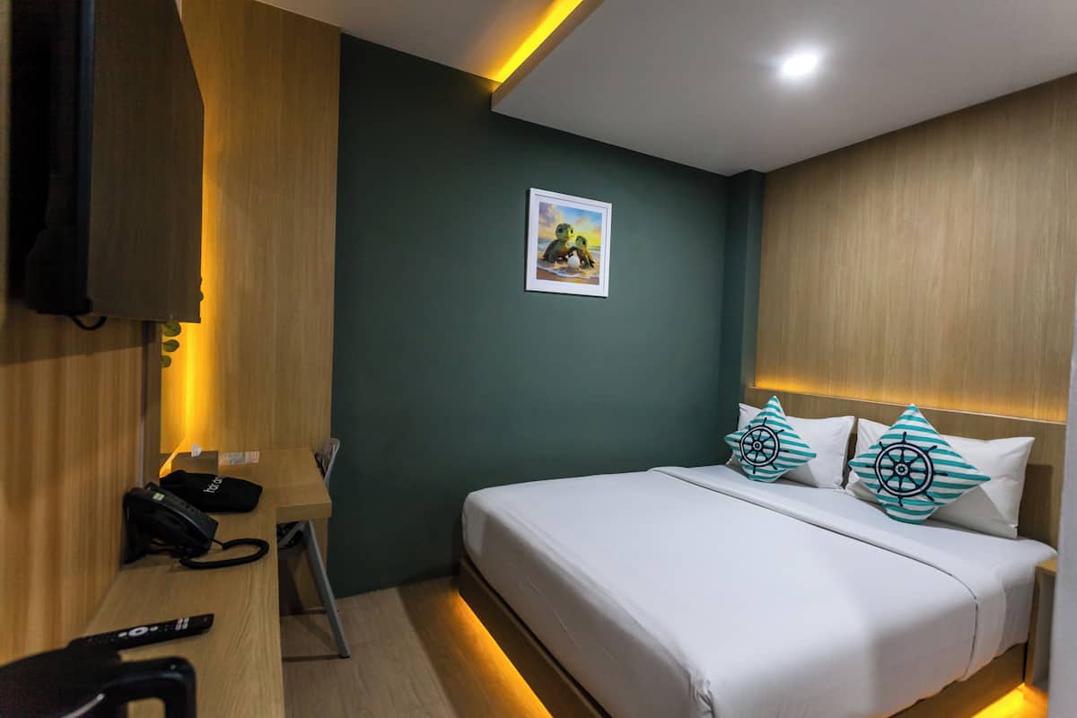 Une chambre d’hôtel équipée d’un lit, d’un bureau, d’un téléphone et d’un téléviseur fixé au mur.
