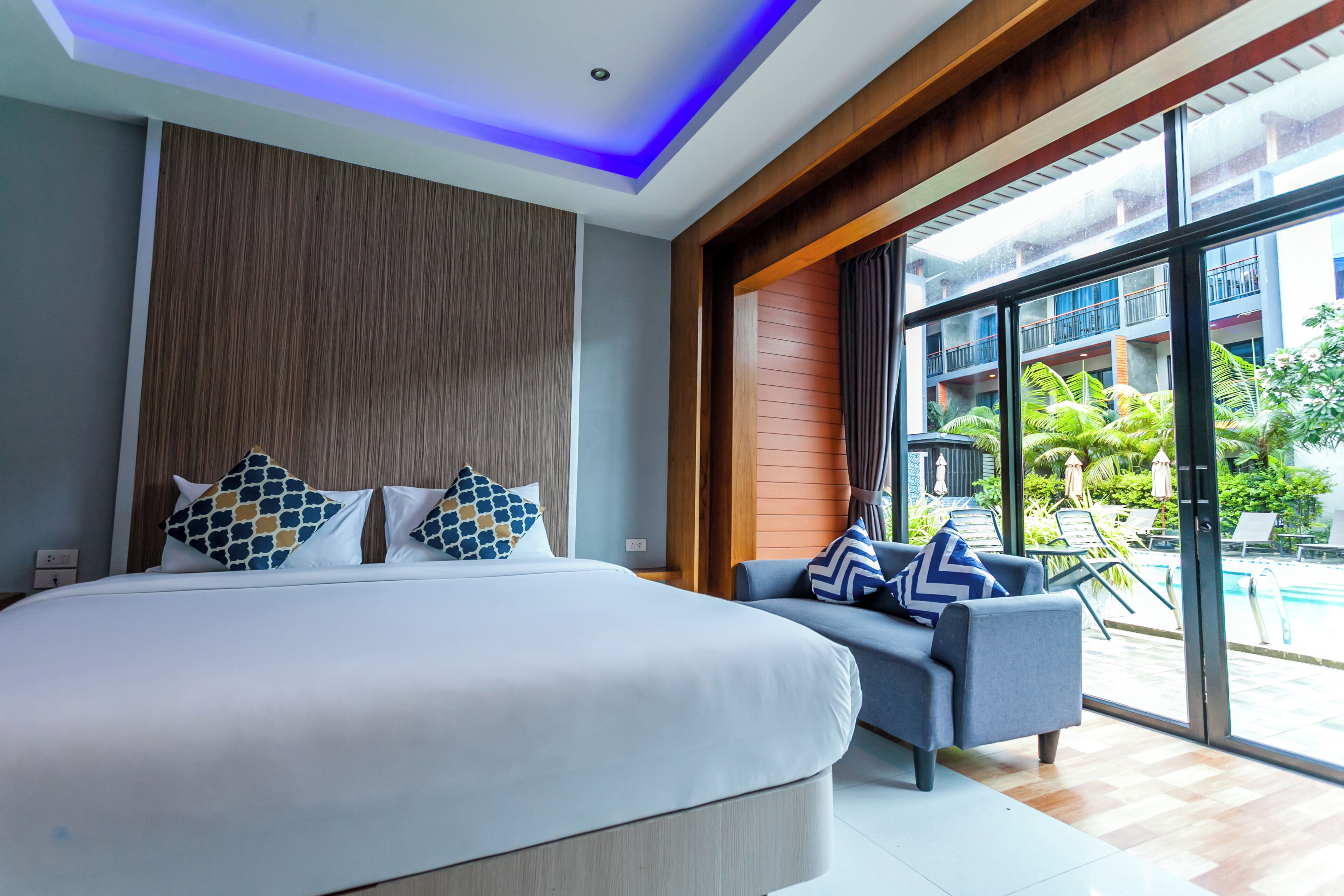 A modern hotel room with a large bed, a sofa, and a balcony with a pool view.