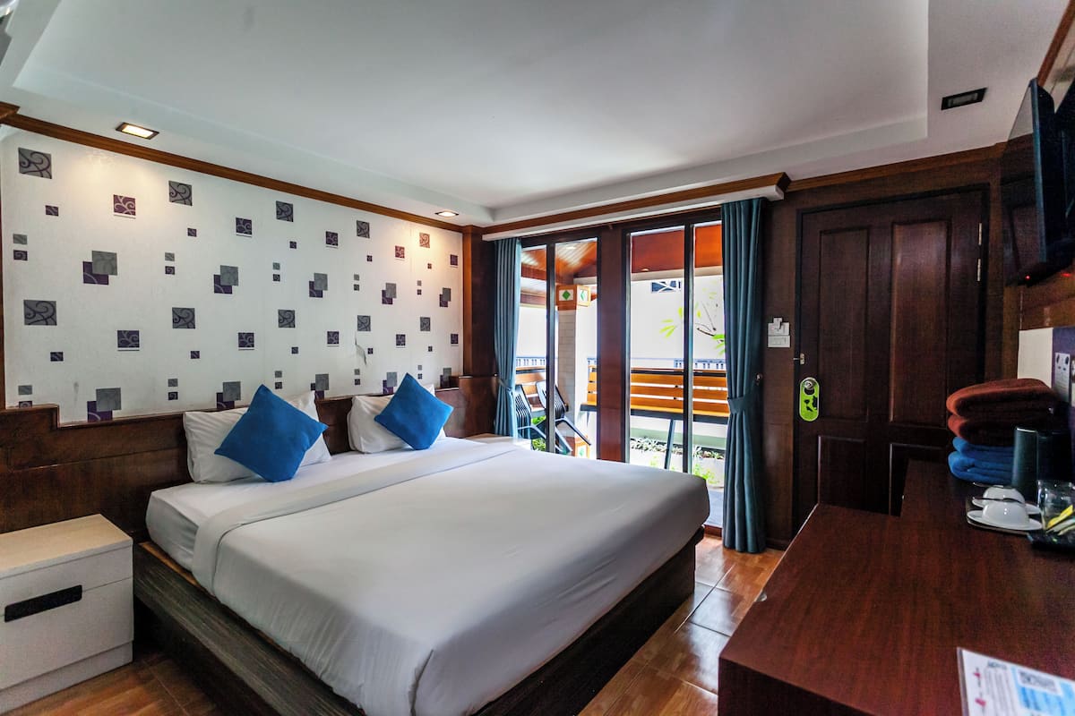 Une chambre d’hôtel avec un grand lit, une tête de lit en bois, un bureau avec une chaise et une vue sur l’extérieur grâce à une porte vitrée.