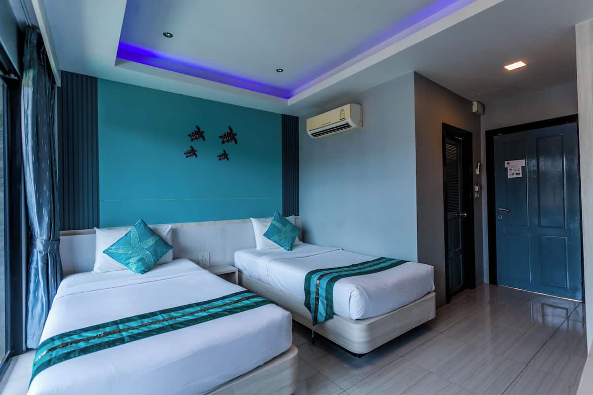 Une chambre d’hôtel avec deux lits, un mur d’accent de couleur turquoise, un appareil de climatisation et une porte avec une pancarte.