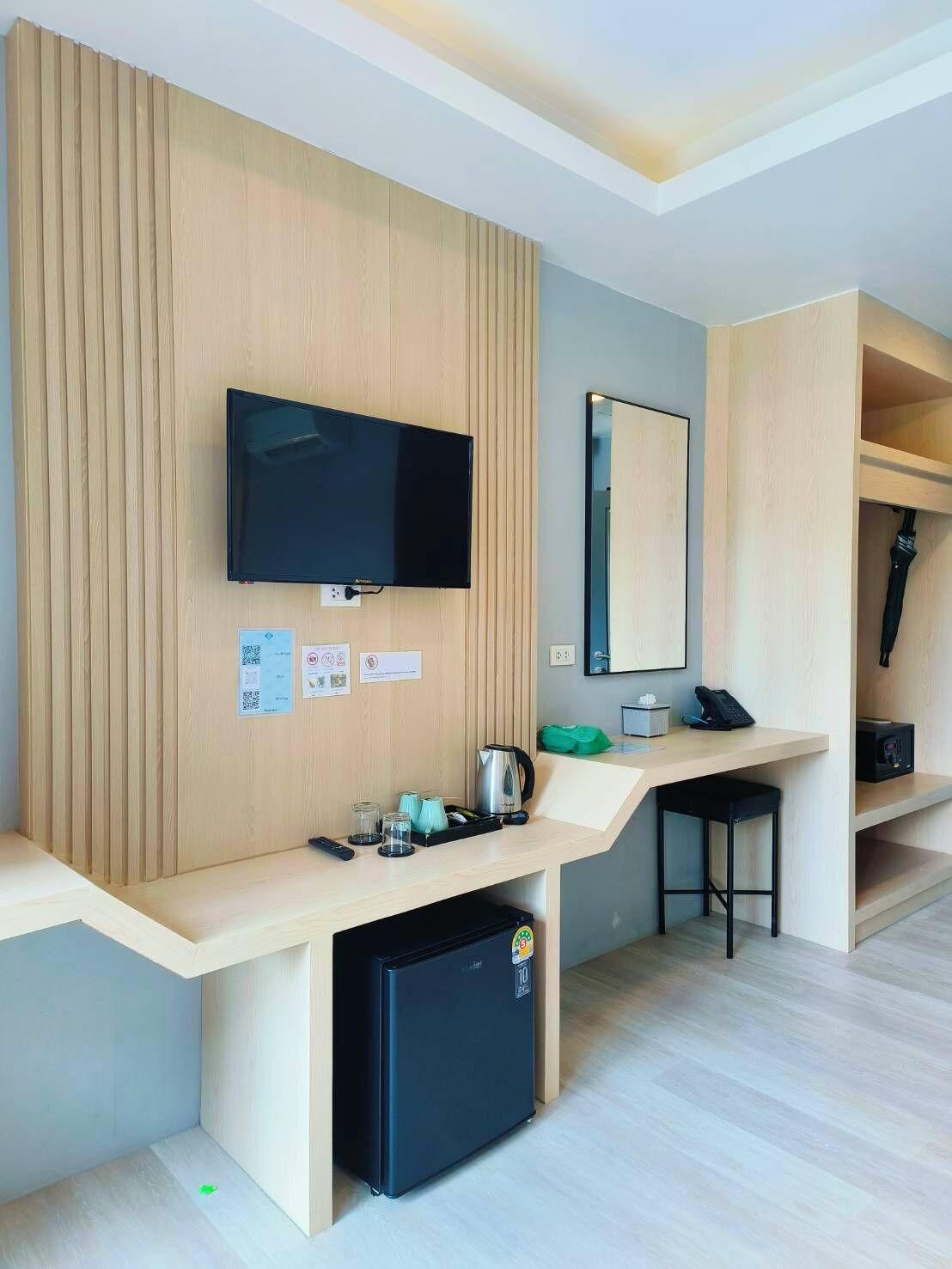 A modern hotel room with a wooden panel wall, a flat-screen TV, a mini-fridge, a coffee maker, and a desk with a chair.