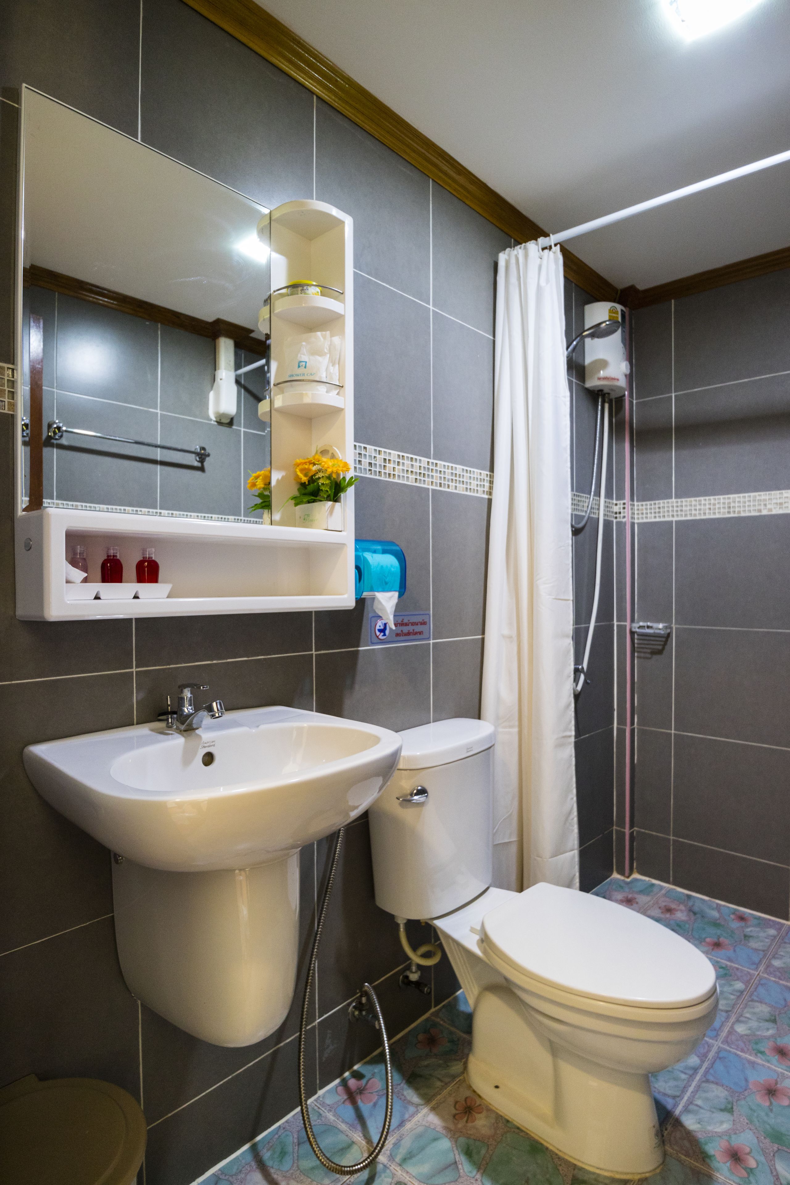 Une salle de bain avec un lavabo, des toilettes et une douche. Il y a un miroir au-dessus du lavabo et une étagère avec des articles de toilette.