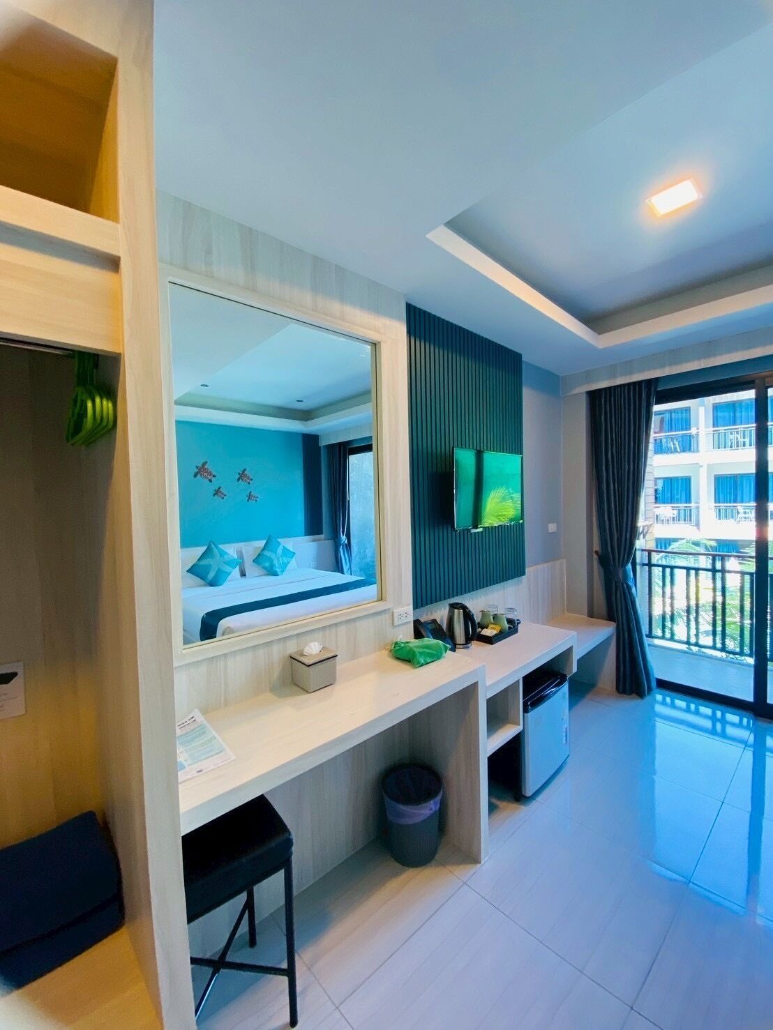 Une chambre d’hôtel moderne dotée d’un grand miroir, d’un téléviseur à écran plat, d’un petit bureau, d’une poubelle et d’un balcon offrant une vue sur la ville.
