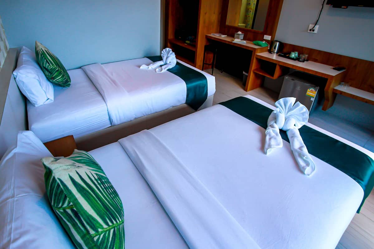 Two beds with crisp linens and a green accent pillow, a compact desk, and a flat-screen TV.