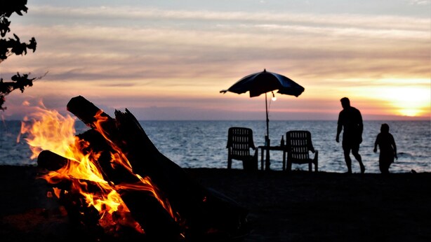 Escena de playa con fuego, dos sillas y una sombrilla.