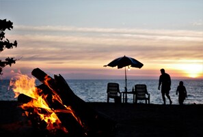 A beach scene with a fire, two chairs, and an umbrella. - Micky Monkey Beach Hotel Phuket Maikhao Thailand (Mai Khao)