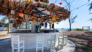 Un bar en la playa con techo de paja, sillas blancas y vista al mar.