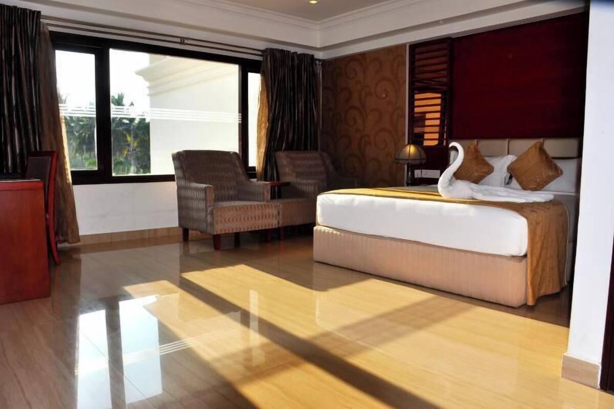 Ein Hotelzimmer mit einem großen Bett, zwei Sesseln, einem Schreibtisch und Blick ins Freie.