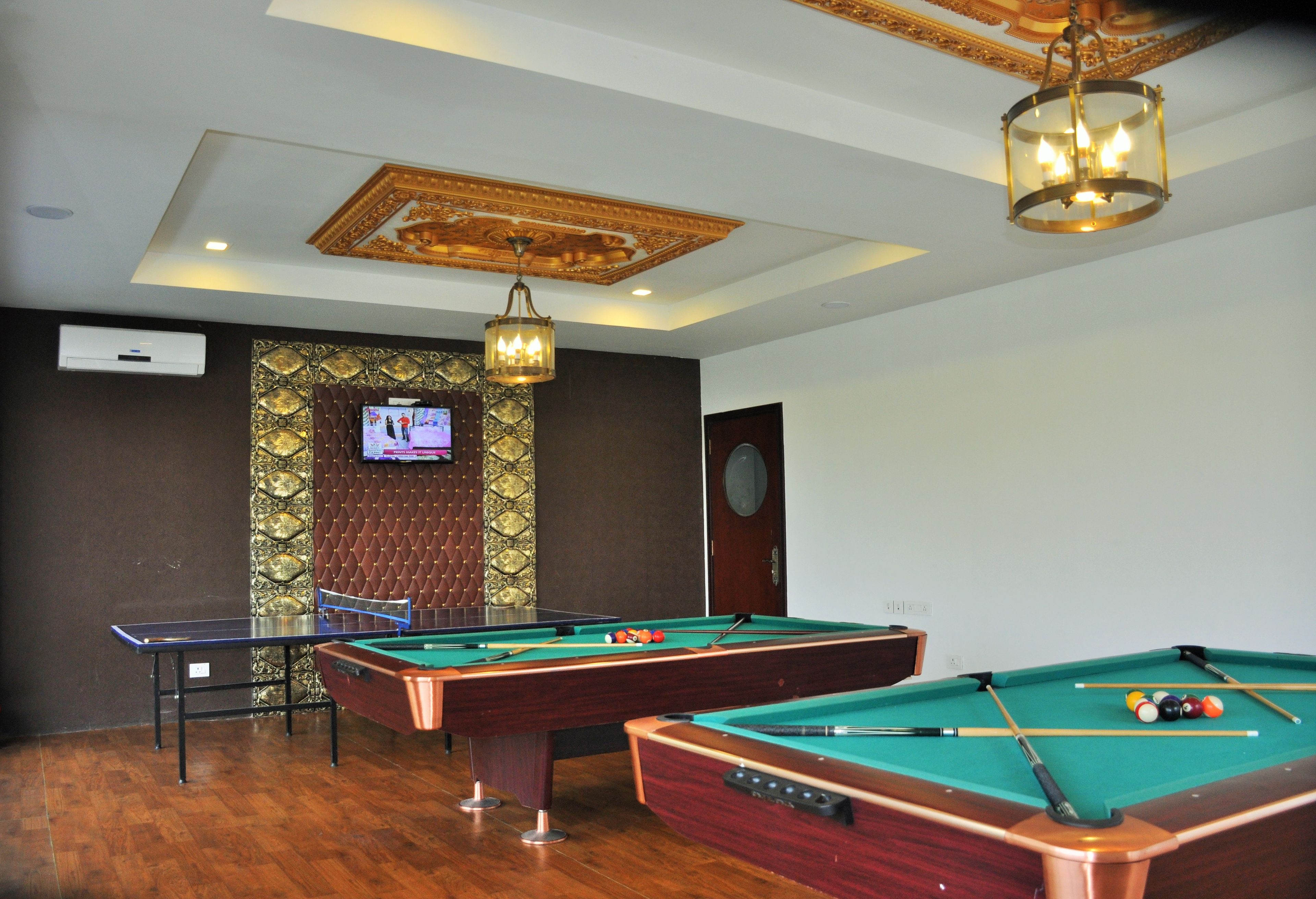 A room with three pool tables, a ping pong table, and a television mounted on a decorative wall.