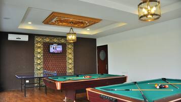 A room with three pool tables, a ping pong table, and a television mounted on a decorative wall.