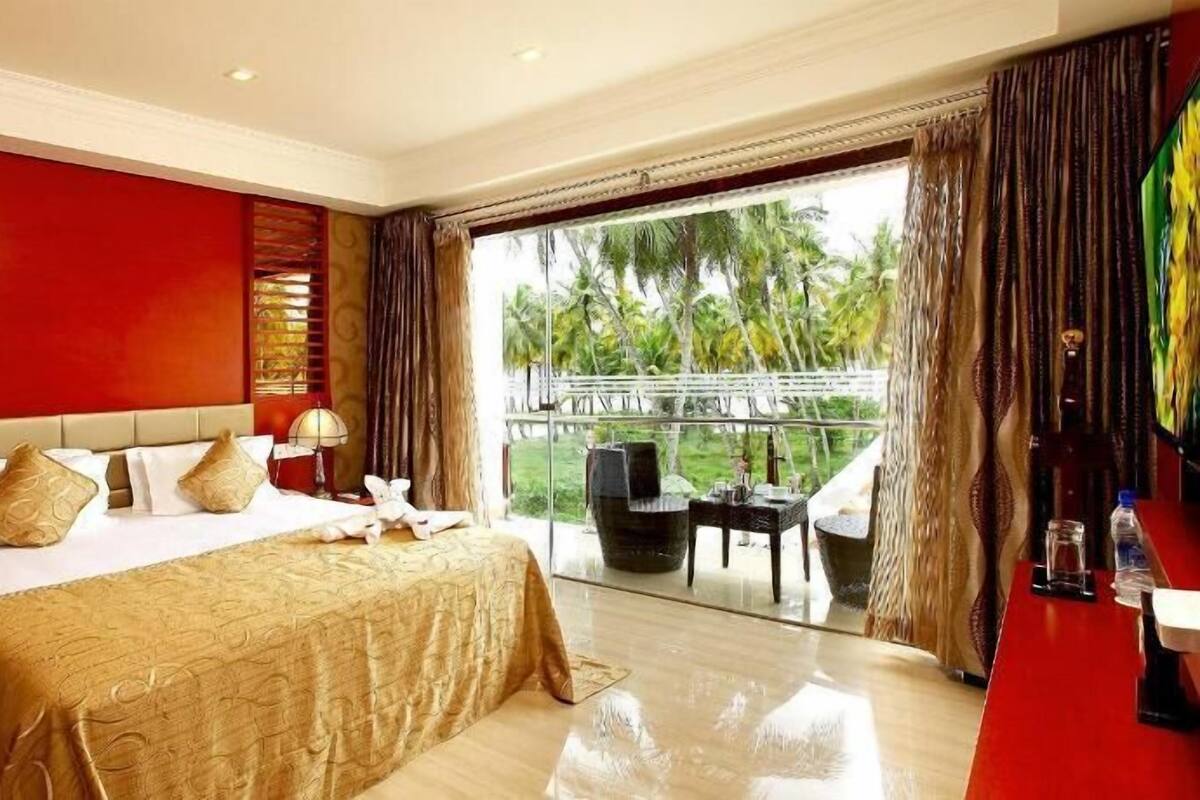 Ein Hotelzimmer mit einem großen Bett, einem Balkon mit Tisch und Stühlen und Blick auf Palmen.