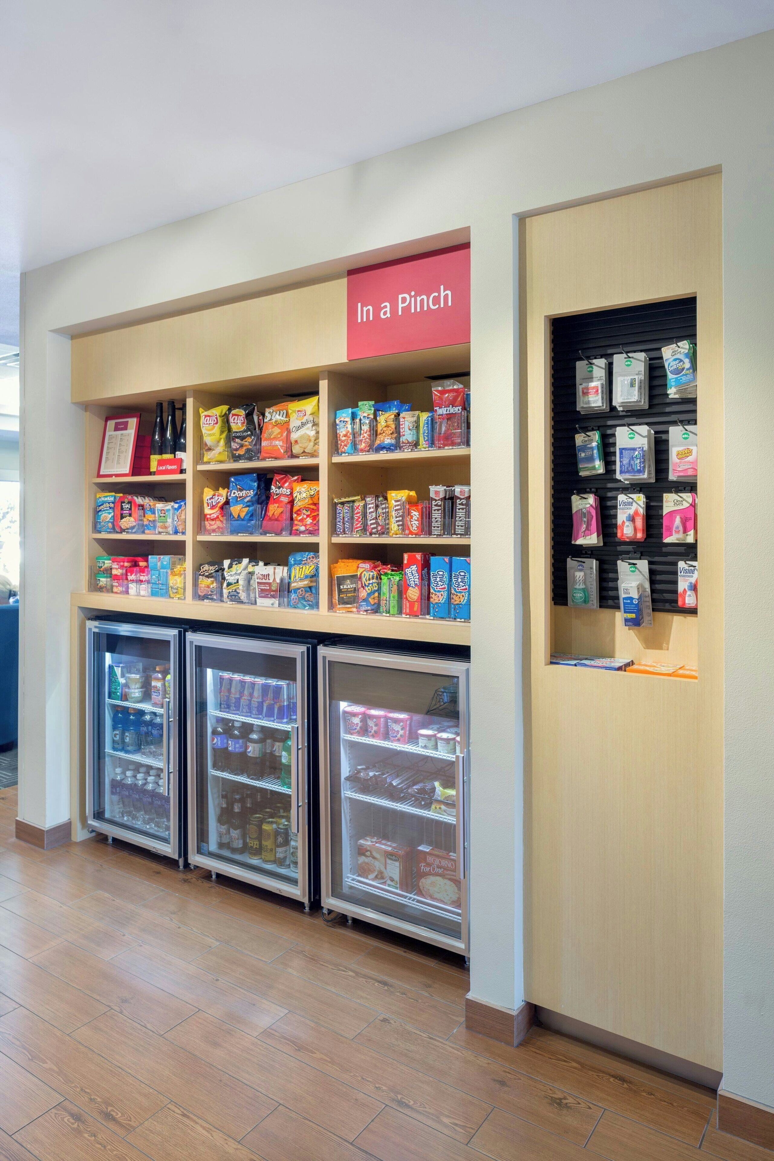 A snack and beverage kiosk with a 'In a Pinch' sign, shelves stocked with snacks and beverages, and refrigerated display cases.