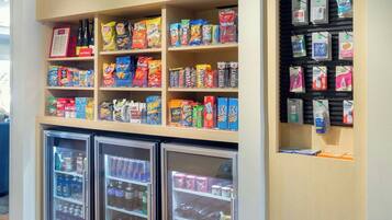 A snack and beverage kiosk with a 'In a Pinch' sign, shelves stocked with snacks and beverages, and refrigerated display cases.