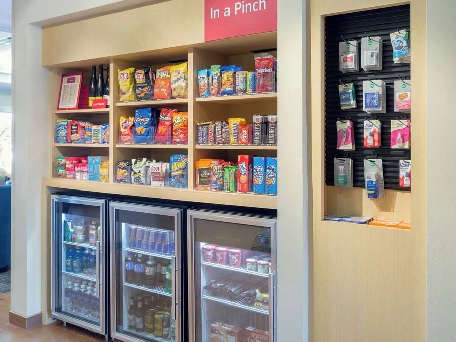 A snack and beverage kiosk with a 'In a Pinch' sign, shelves stocked with snacks and beverages, and refrigerated display cases.