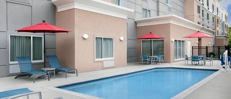 A hotel pool area with lounge chairs and red umbrellas.