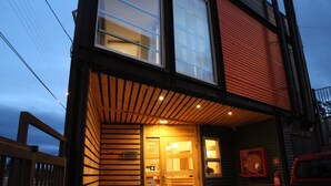A building with a reception area, wooden slats on the facade, and a red vehicle parked outside. - Apart Hotel Quillango (Punta Arenas)