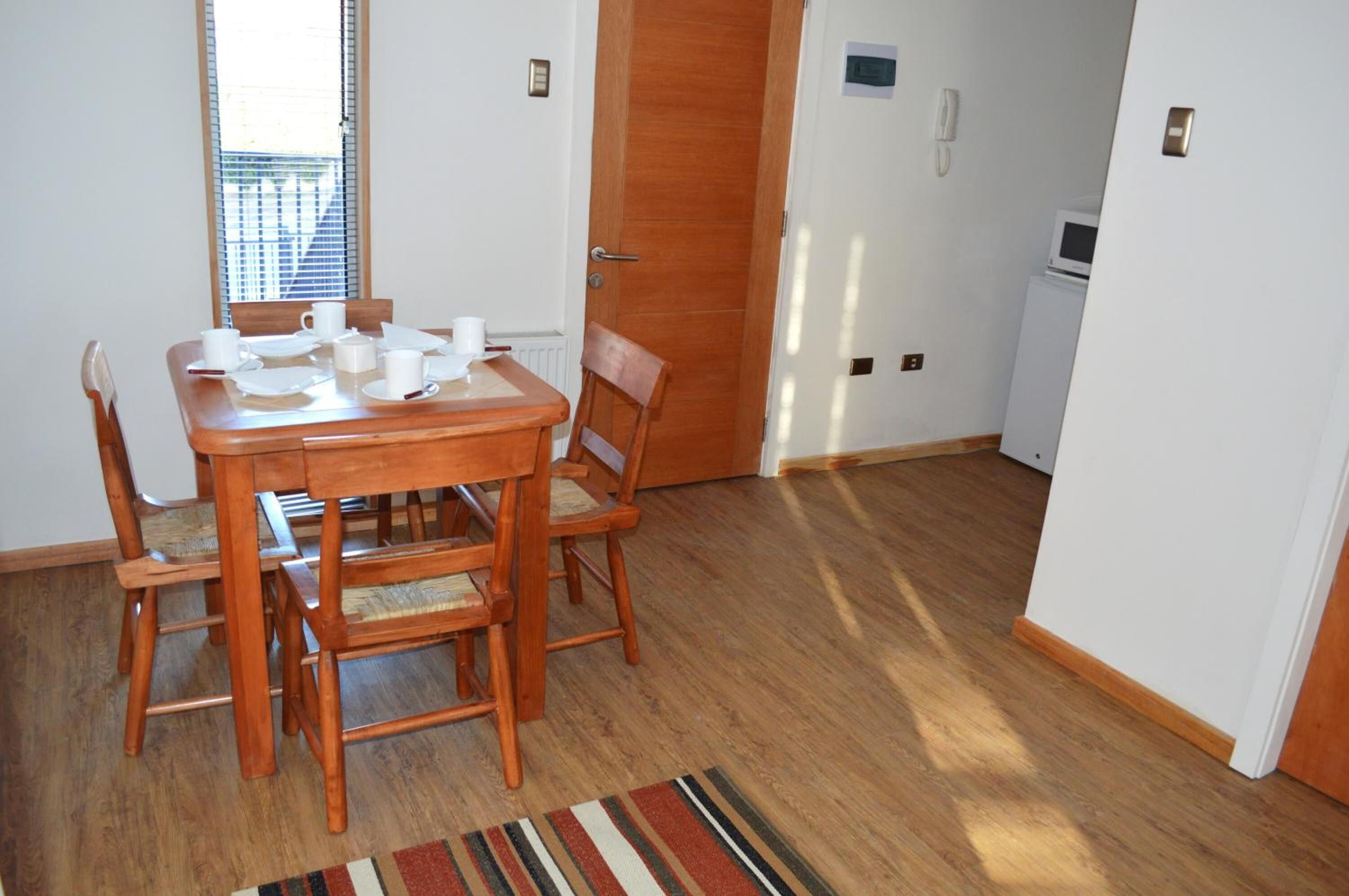 A dining area with a wooden table and chairs, a striped rug, and a door leading to a kitchen.