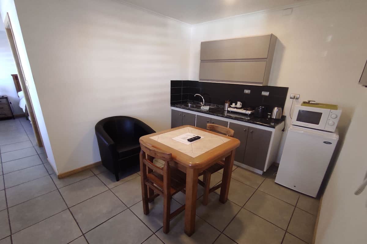 Uma cozinha compacta com uma mesa de jantar e cadeiras, uma cadeira preta, um micro-ondas e um frigorífico pequeno.