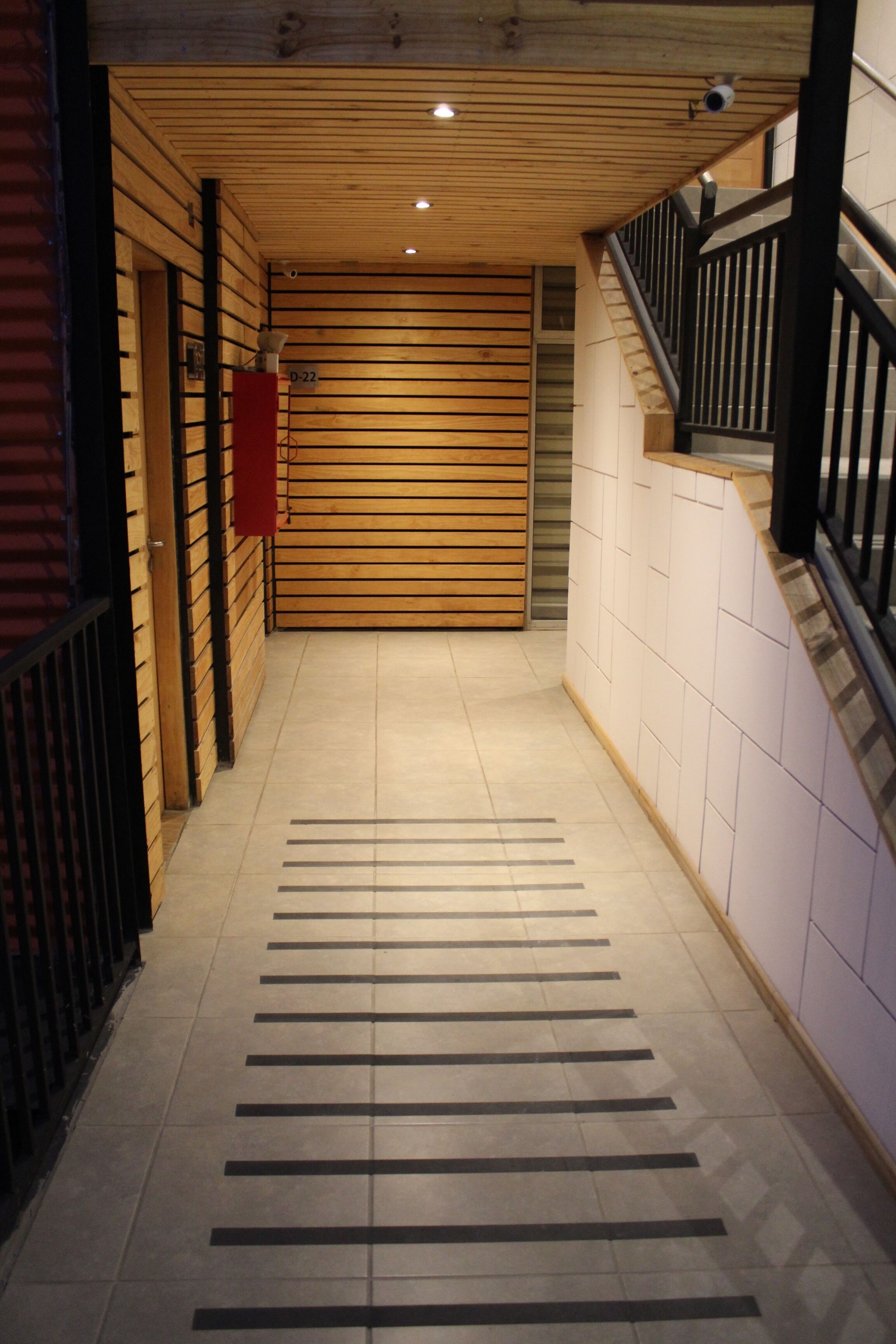 A hallway with wooden slats on the walls, a tiled floor, and a staircase with a black railing.