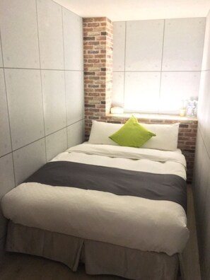 A small, modern bedroom with a brick accent wall, a window with a view, and a bed with a green pillow. - TO Hotel Chengde (Taipei)