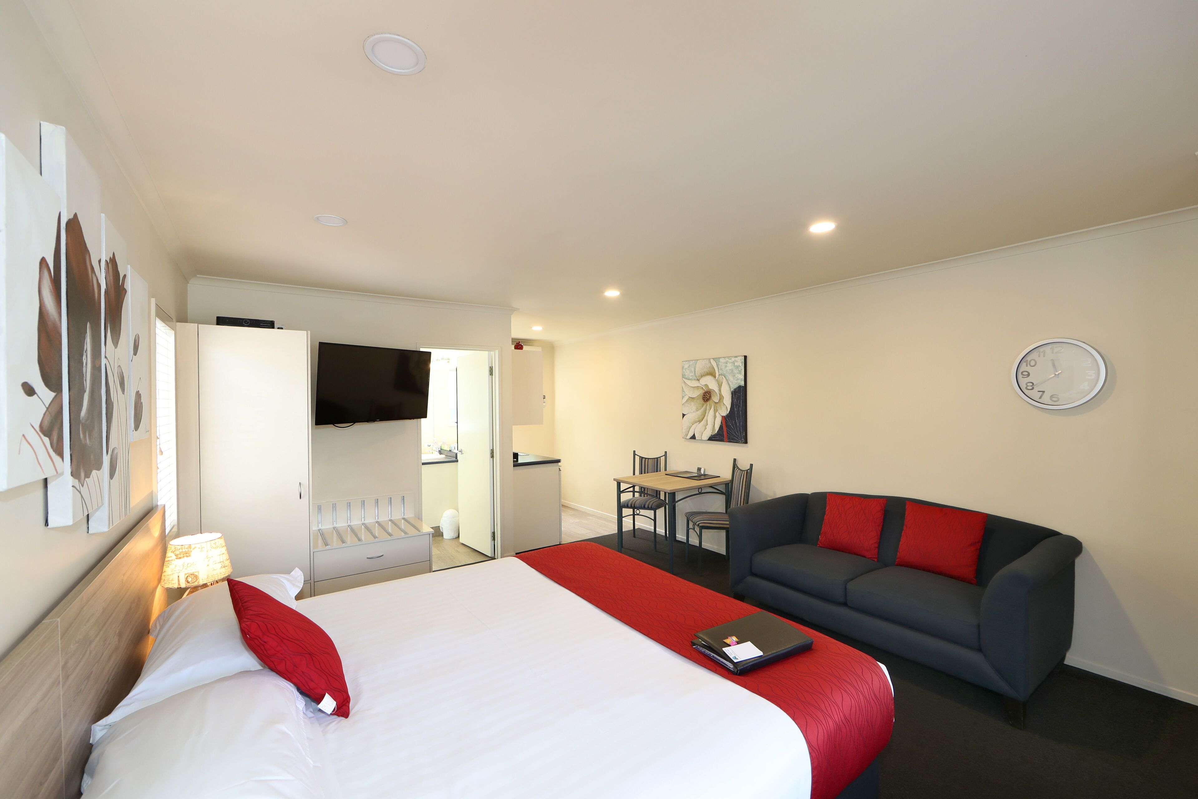 Une chambre d’hôtel avec un lit, un canapé rouge et noir, un coin repas et un téléviseur.
