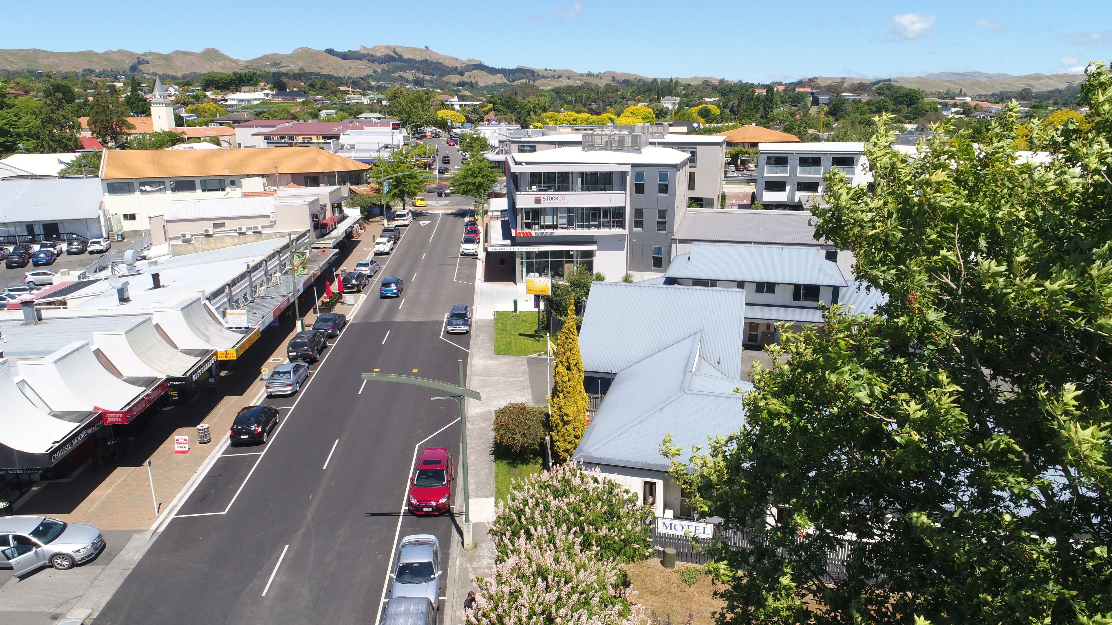 A street view with a motel, a parking lot, and buildings with flat roofs.