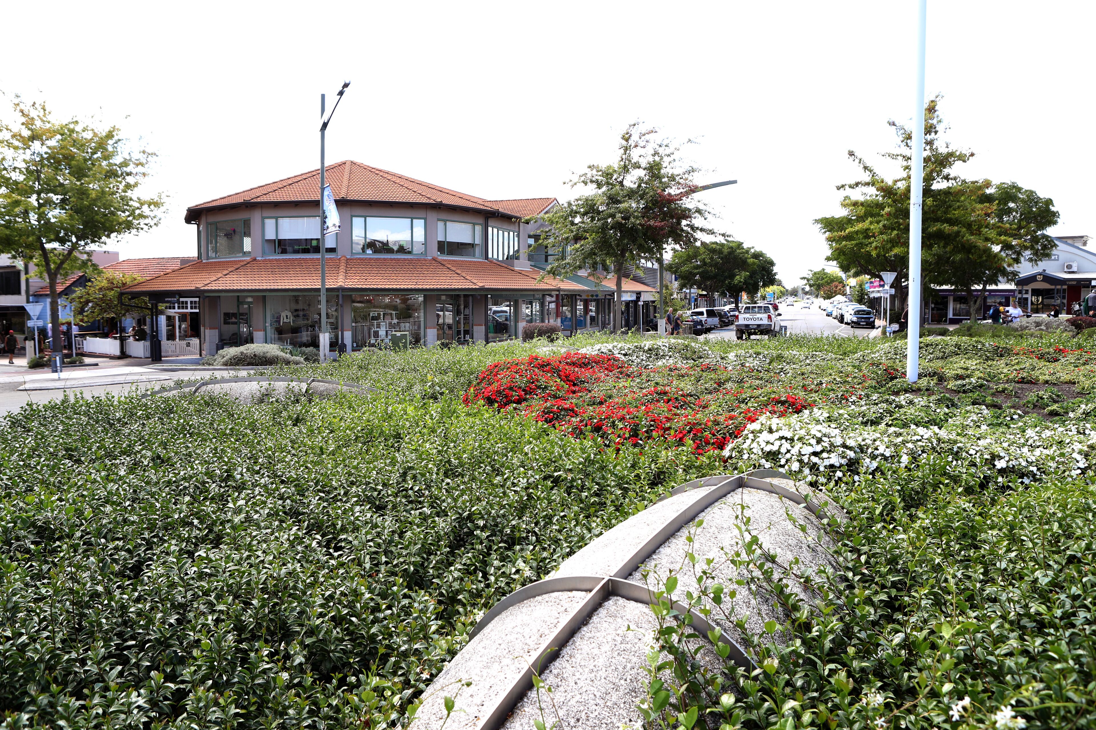 Um edifício com telhado de telhas vermelhas, rodeado por um jardim ajardinado com flores vermelhas e arbustos verdes.
