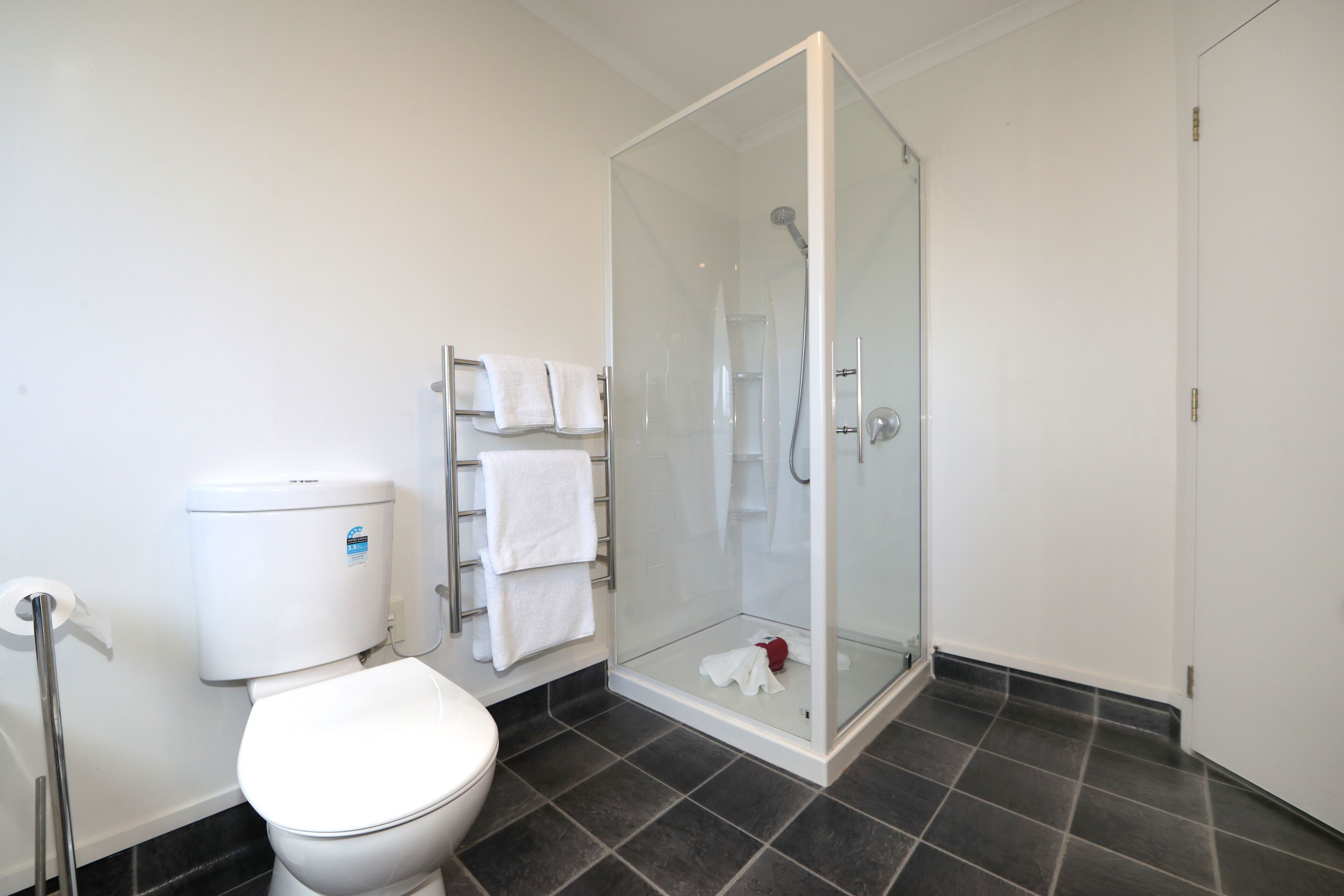 Un baño moderno con ducha de vidrio, inodoro y toallero con varias toallas.