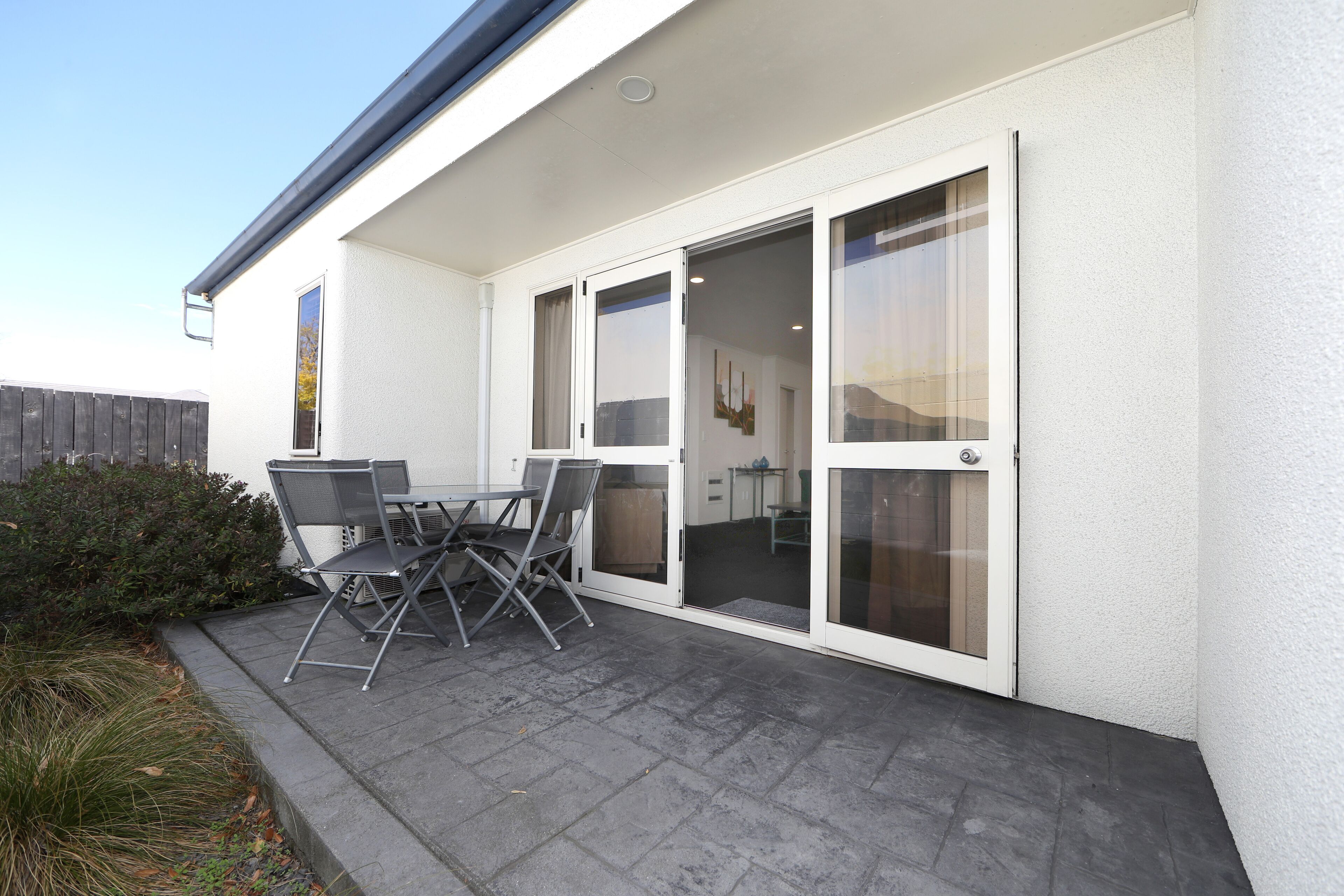 A patio with a table and chairs, a sliding glass door, and a wooden fence.