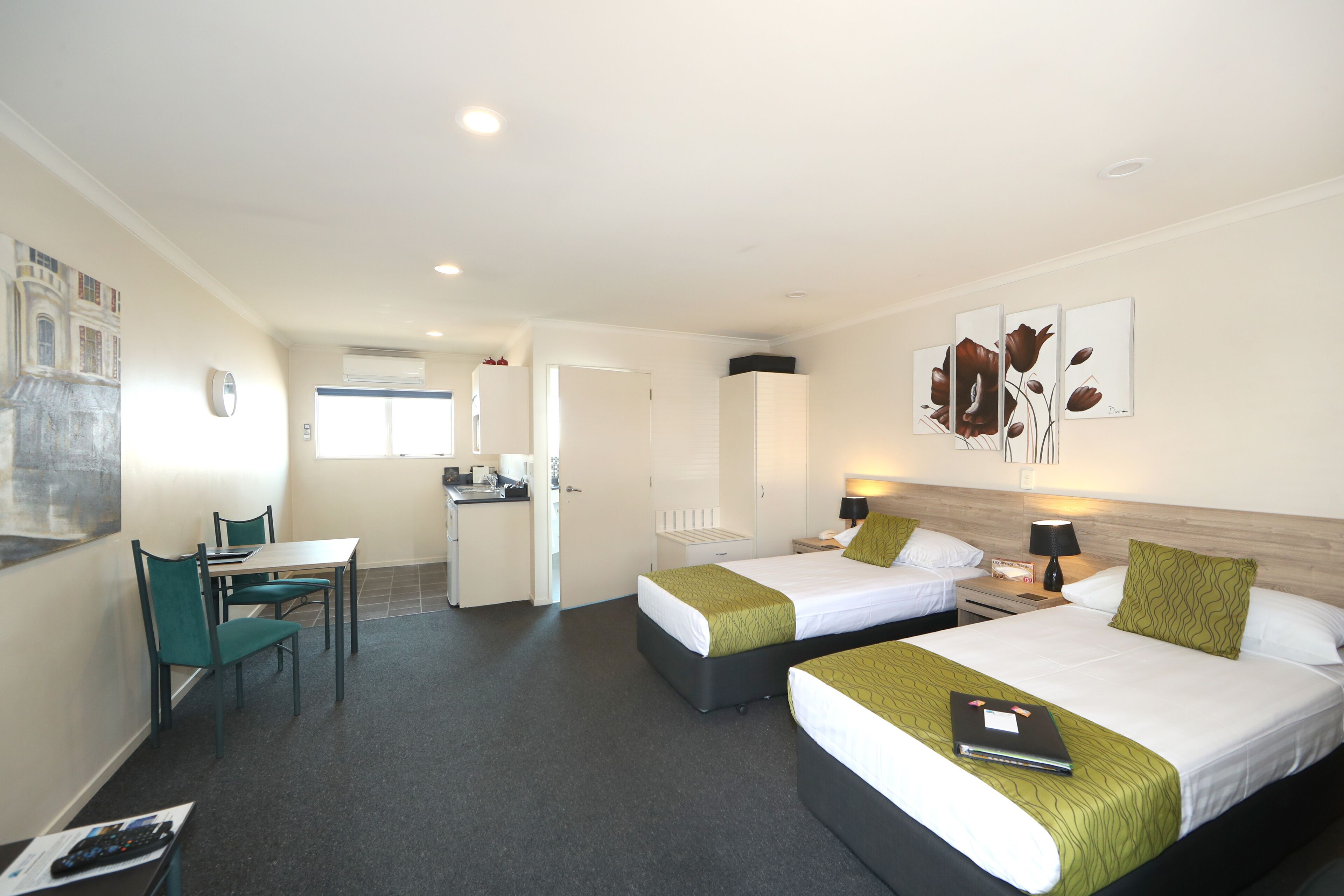 A hotel room with two beds, a desk, and a kitchenette.