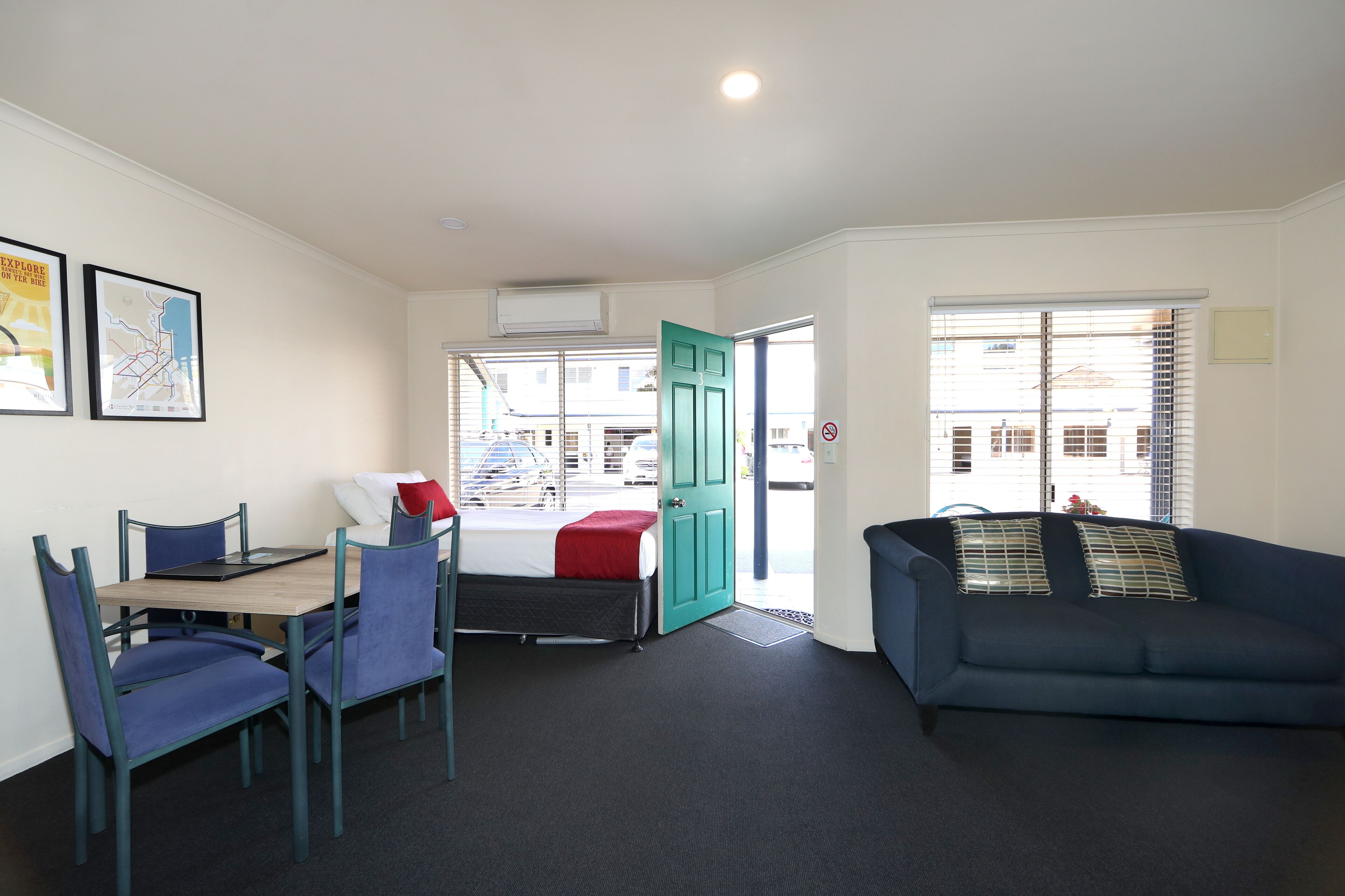 A room with a bed, a desk with a chair, a sofa, and a window with blinds.