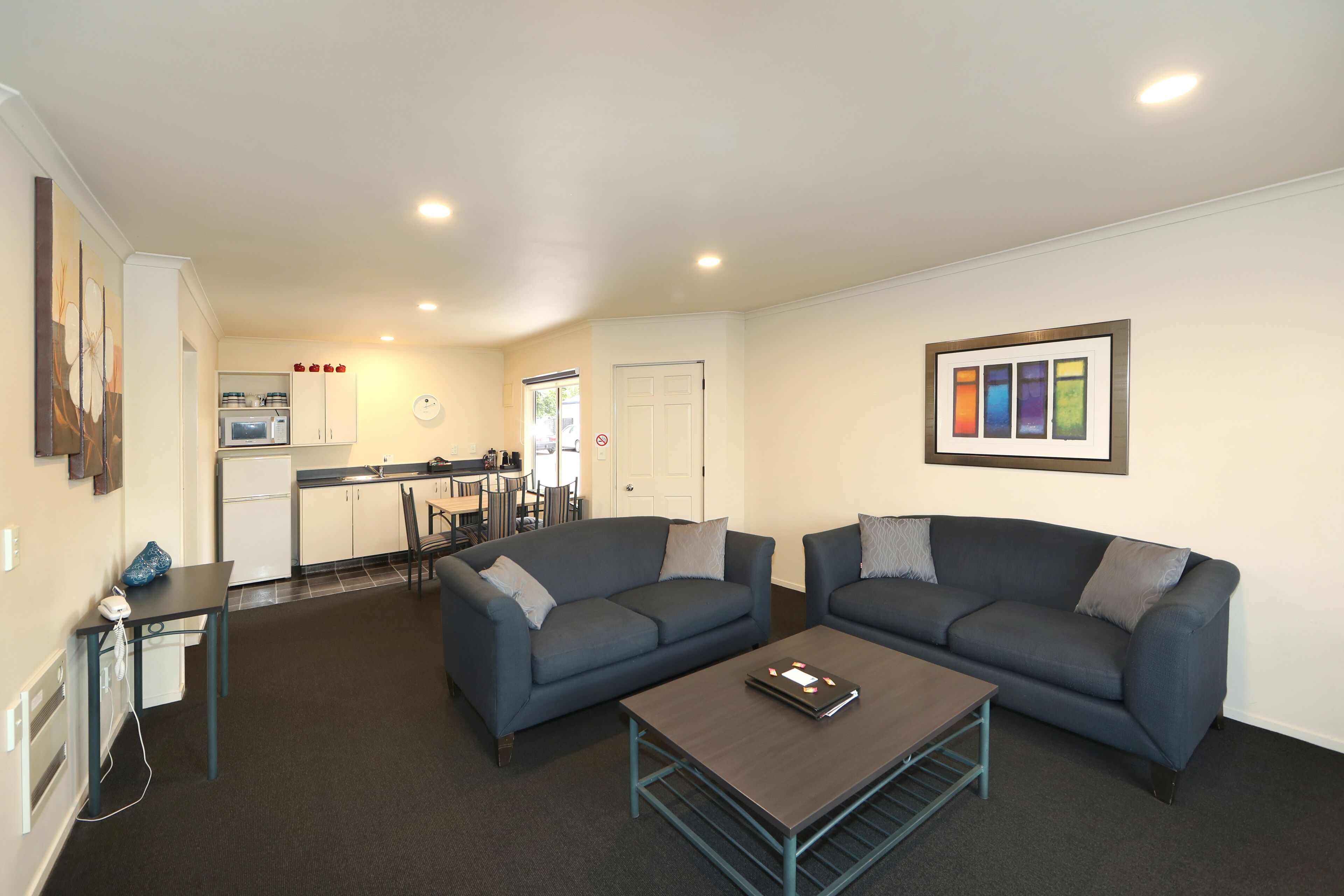 A living area with two sofas, a coffee table, and a kitchen in the background.
