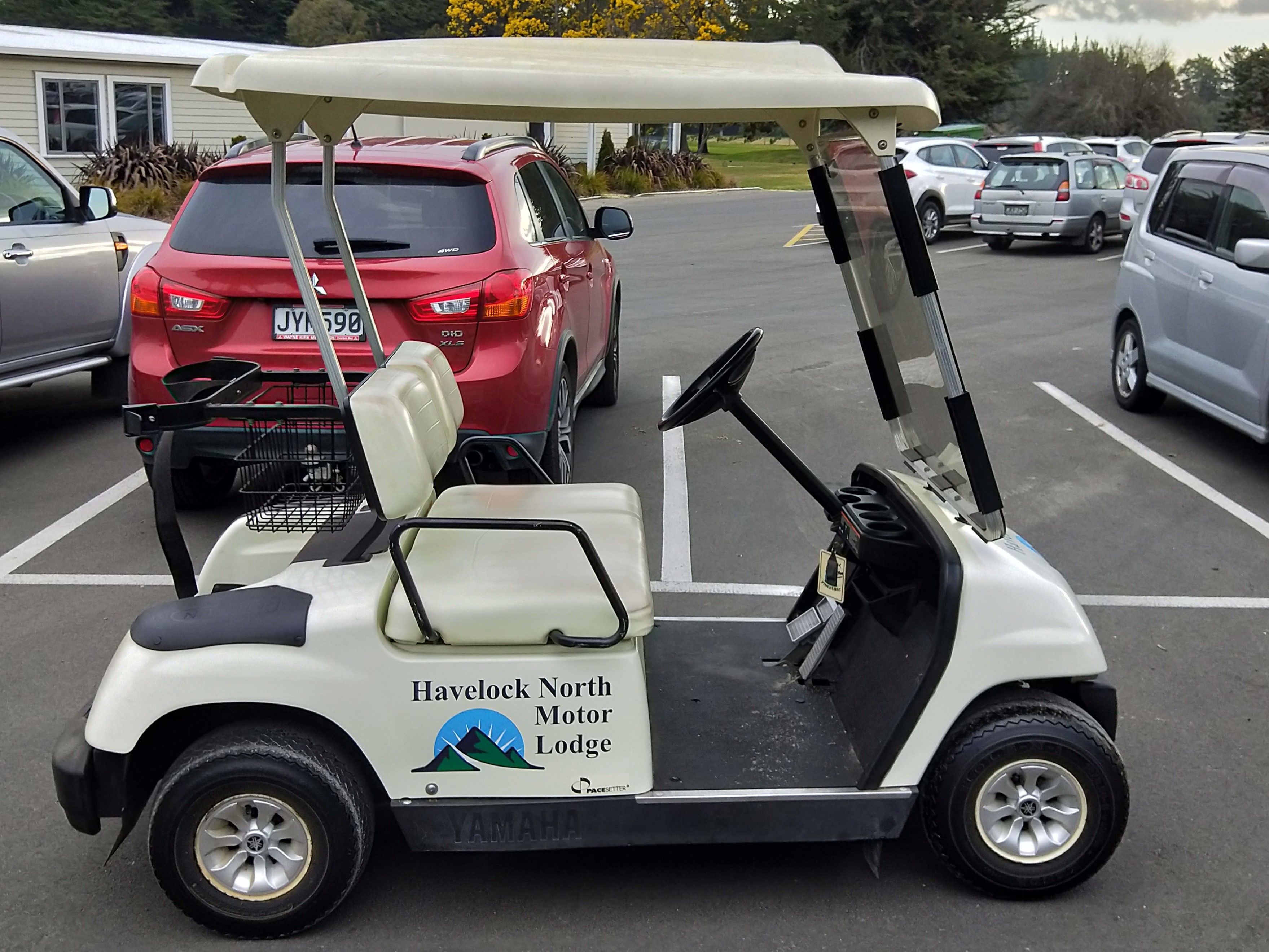 Um carrinho de golfe com a marca 'Havelock North Motor Lodge' estacionado em um estacionamento.