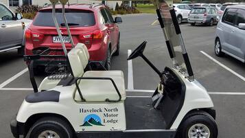 Um carrinho de golfe com a marca 'Havelock North Motor Lodge' estacionado em um estacionamento.