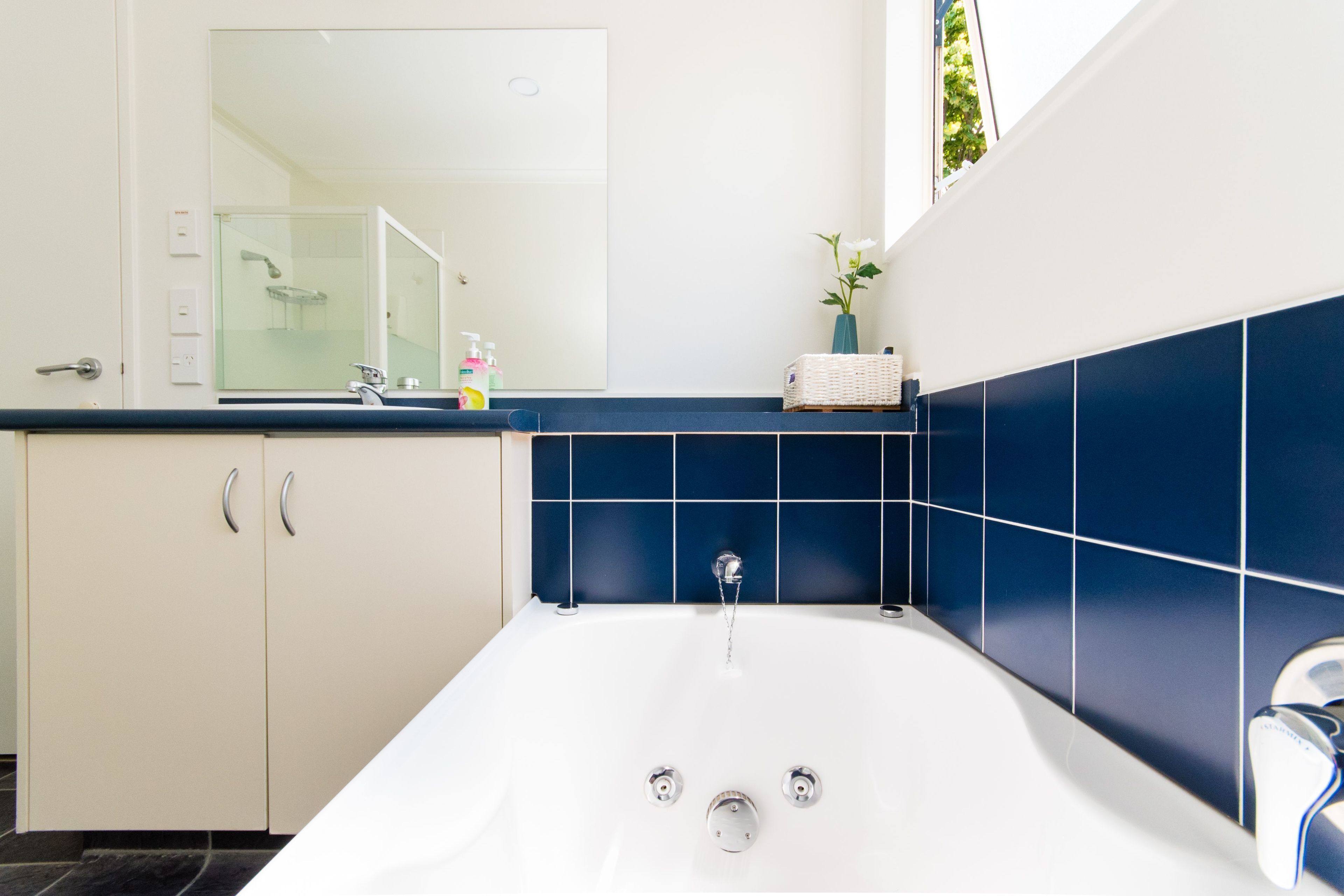 A modern bathroom with a white bathtub, a large mirror, and blue tiles.