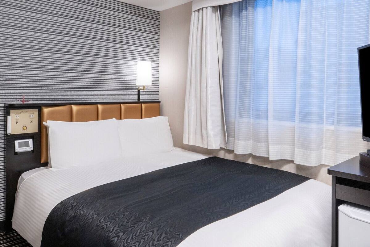 Ein Hotelzimmer mit Bett, Fernseher, Schreibtisch und Bedienfeld an der Wand.
