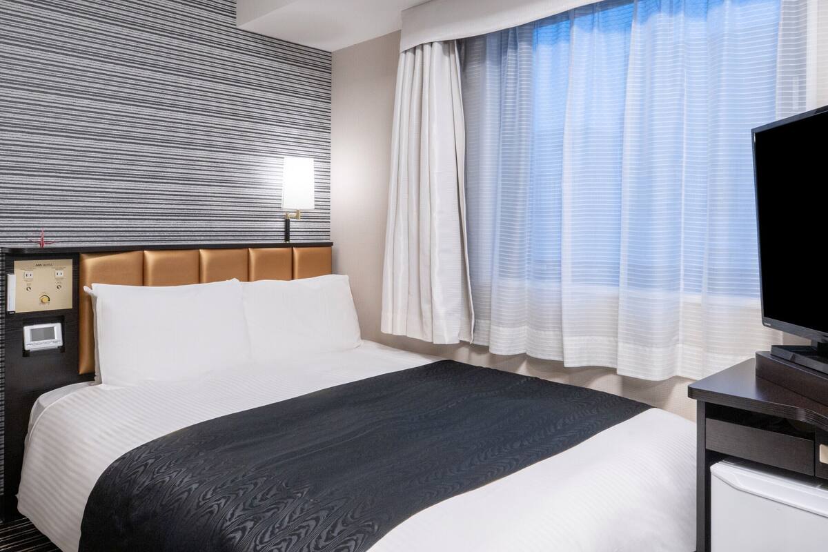 Ein Hotelzimmer mit einem Bett, einem Nachttisch, einem Fernseher und einem Fenster mit Vorhängen.
