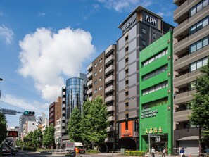 Un immeuble à plusieurs étages doté d’une façade verdoyante et d’une enseigne indiquant « APA HOTEL » et « OH-NISHI ALL SEASON’S DECORATION ».
