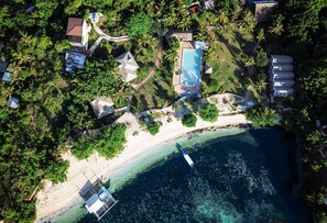 An aerial view of a coastal area with a beach, clear blue water, and a boat docked near the shore. - Thresher Cove Dive Resort (Daanbantayan)
