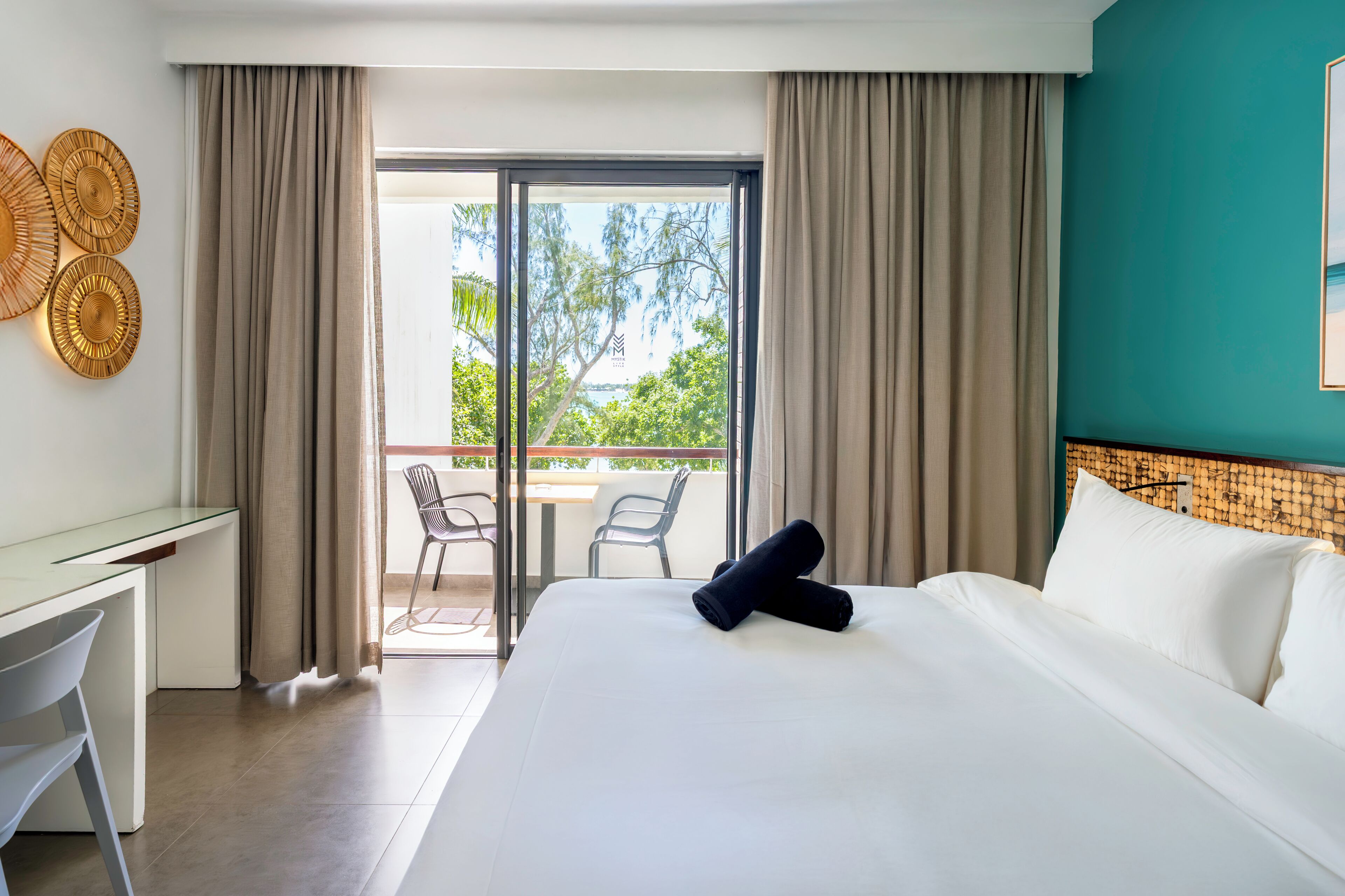 Una camera d'albergo con un letto, una scrivania e un balcone con sedie.