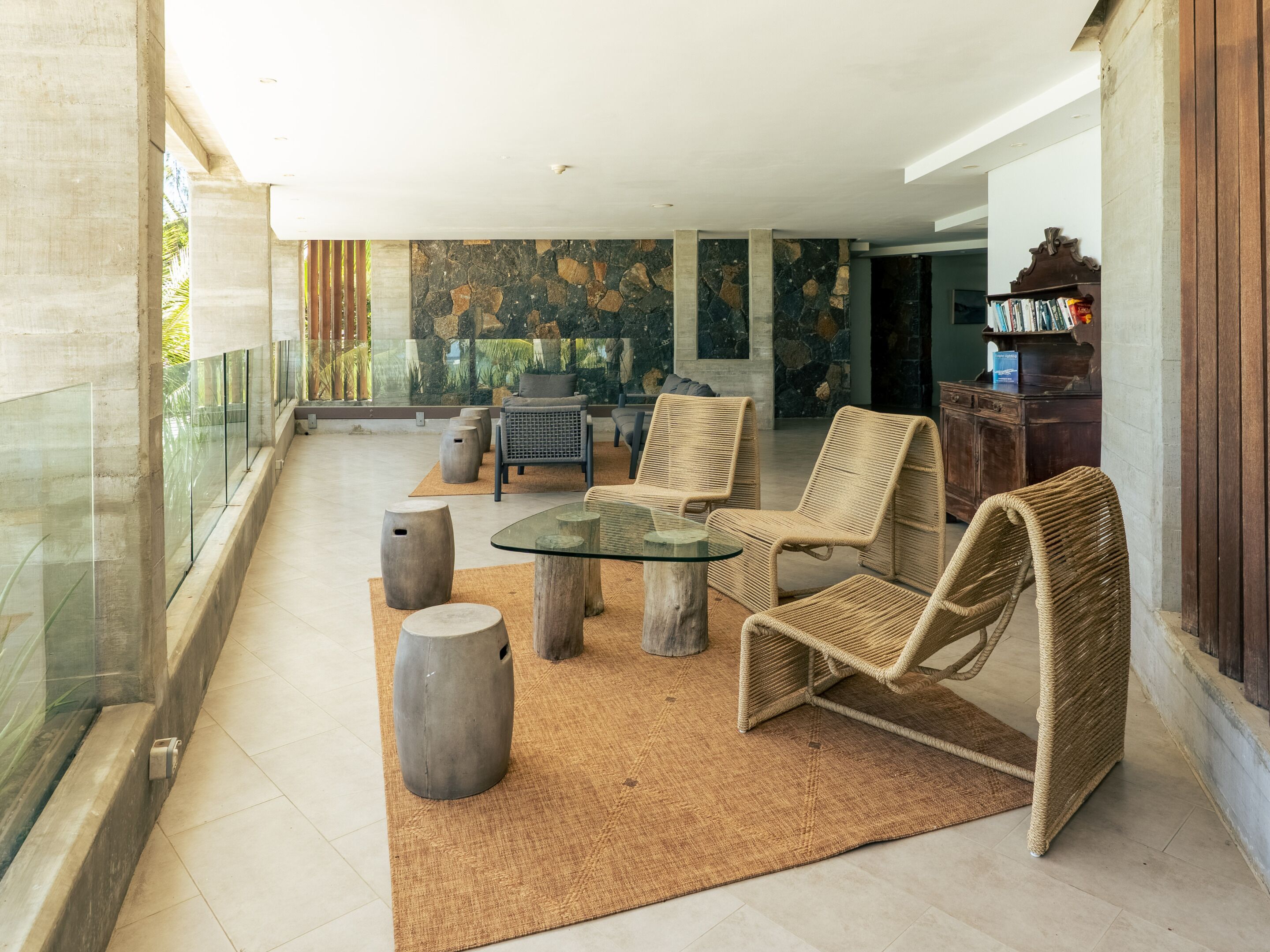 A spacious indoor area with a glass railing, wicker furniture, a stone wall, and a wooden cabinet with books.