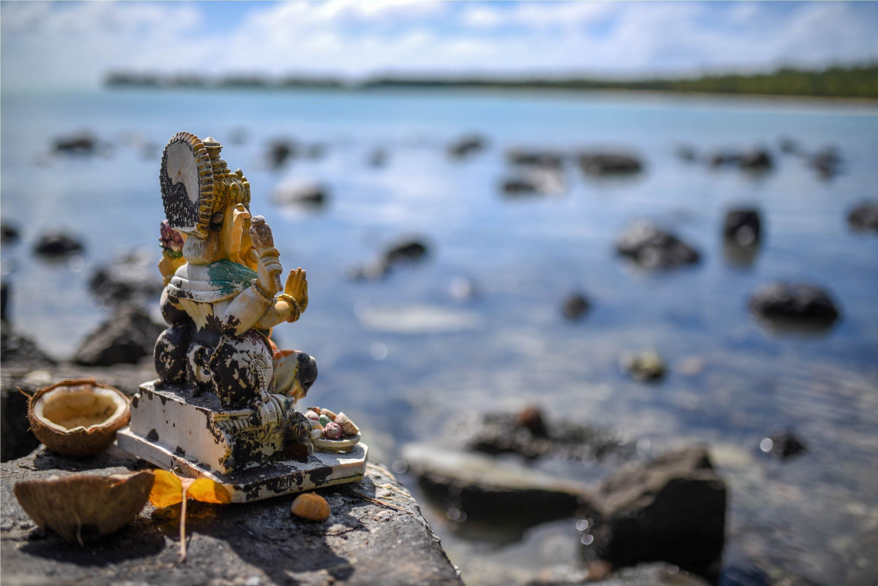 A small statue on a rock by a body of water.