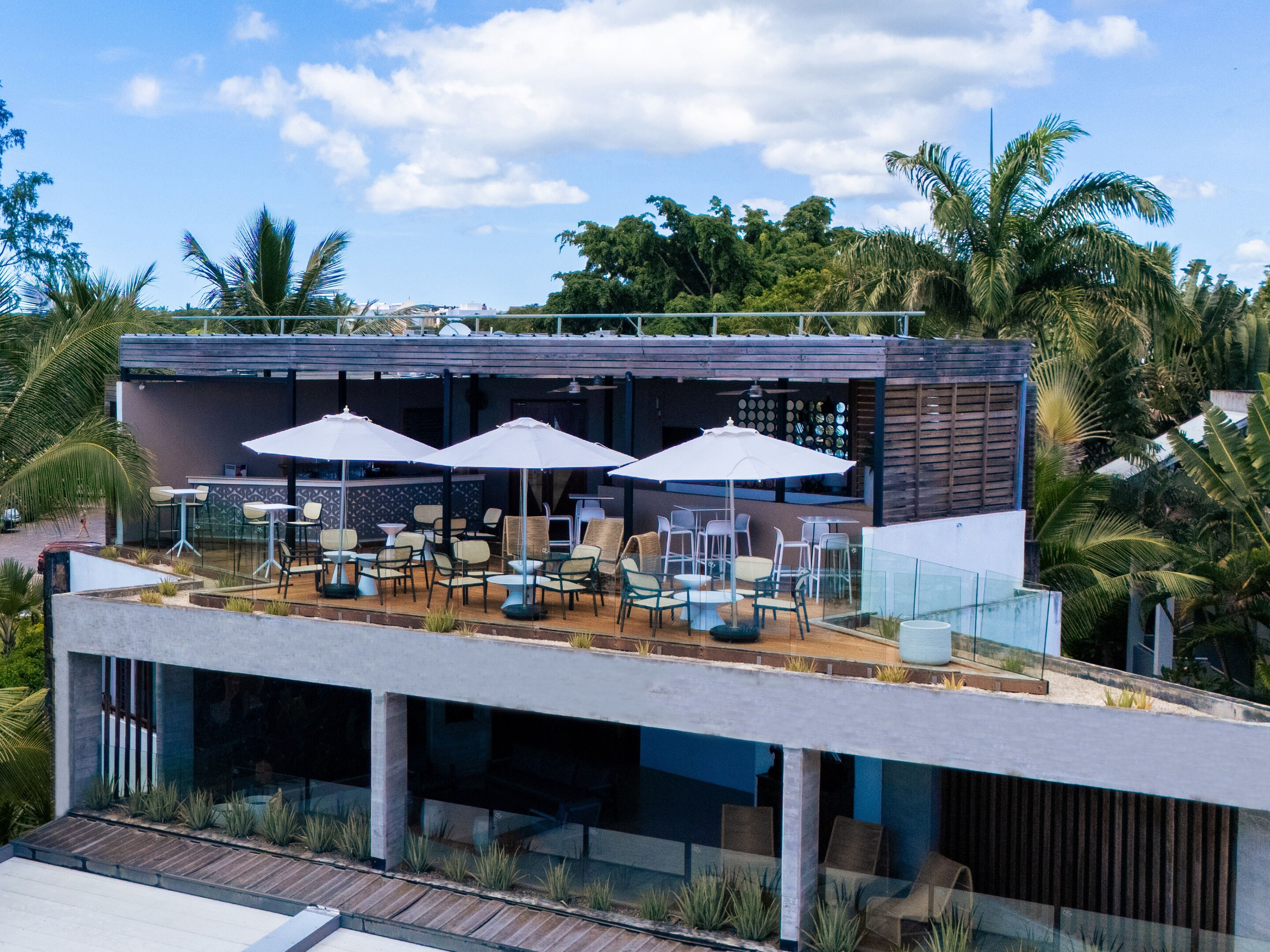 A modern outdoor seating area with umbrellas and chairs, overlooking a pool and lush greenery.