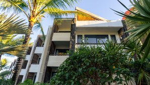 Un edificio de varios pisos con balcones, rodeado de exuberante follaje y palmeras.