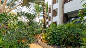 Un sendero bordeado por abundante vegetación y un edificio moderno con balcones.