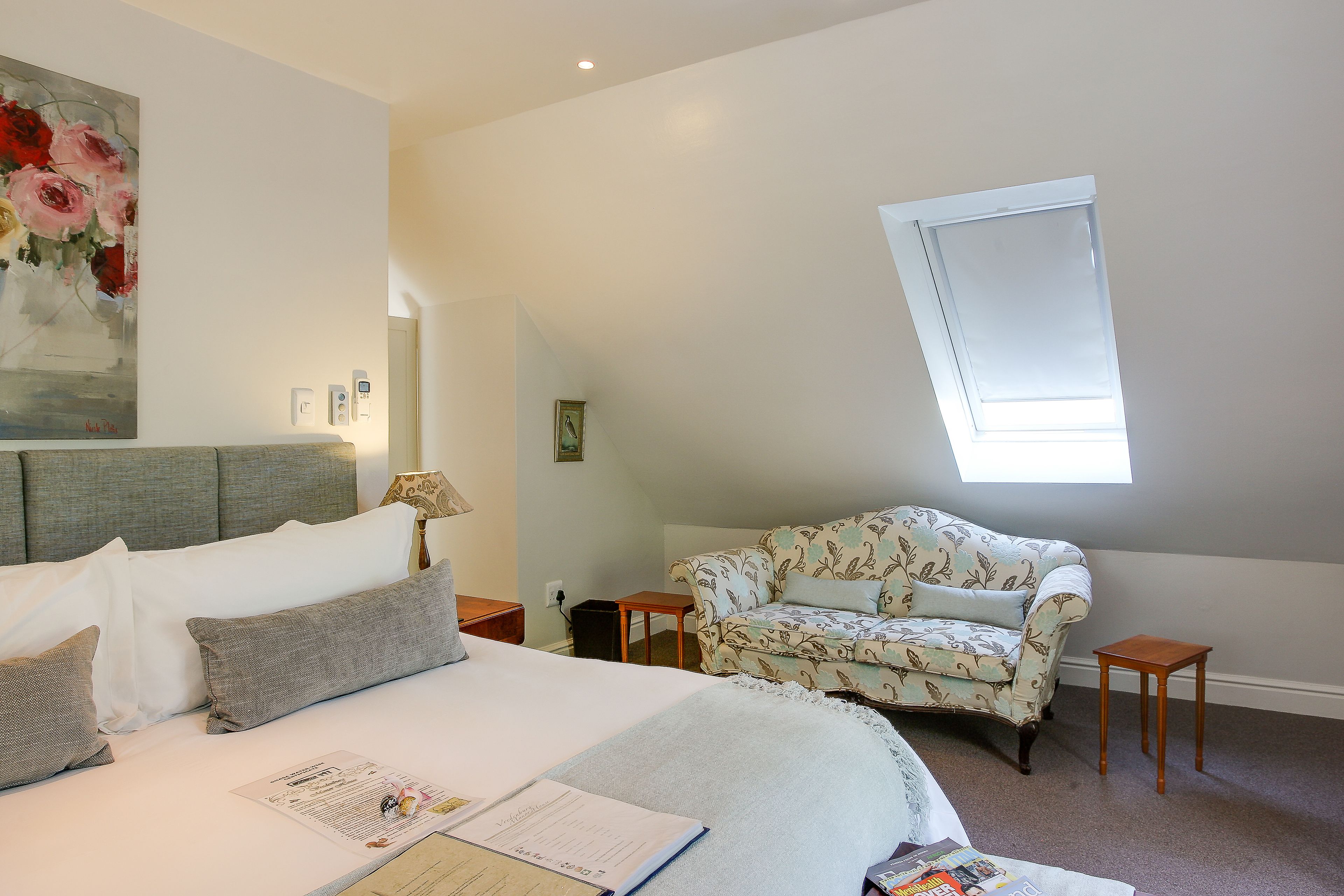 A bedroom with a bed, a floral armchair, a small table, and a window.
