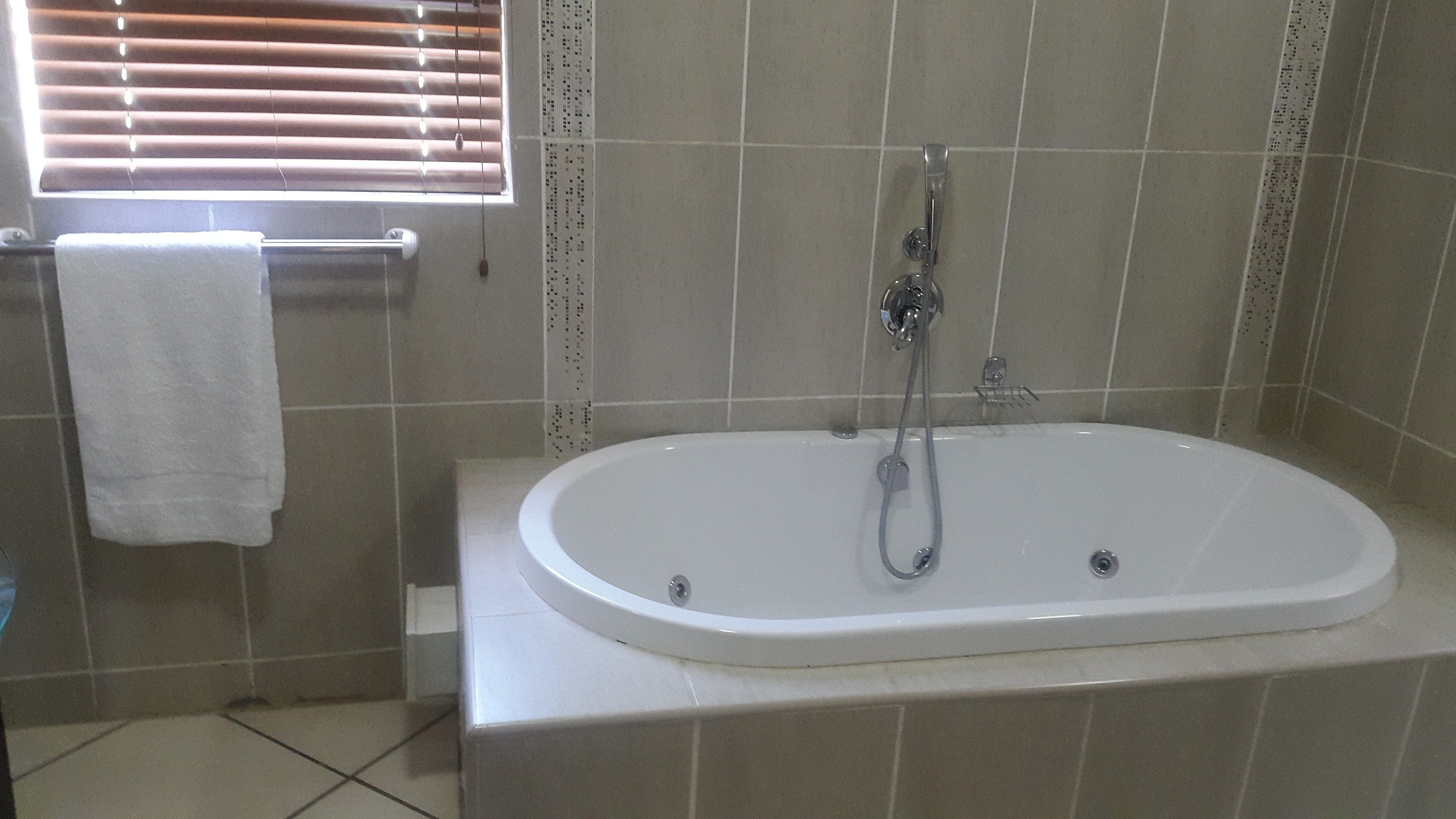 Uma casa de banho com banheira branca, janela com persianas e paredes revestidas a azulejos.